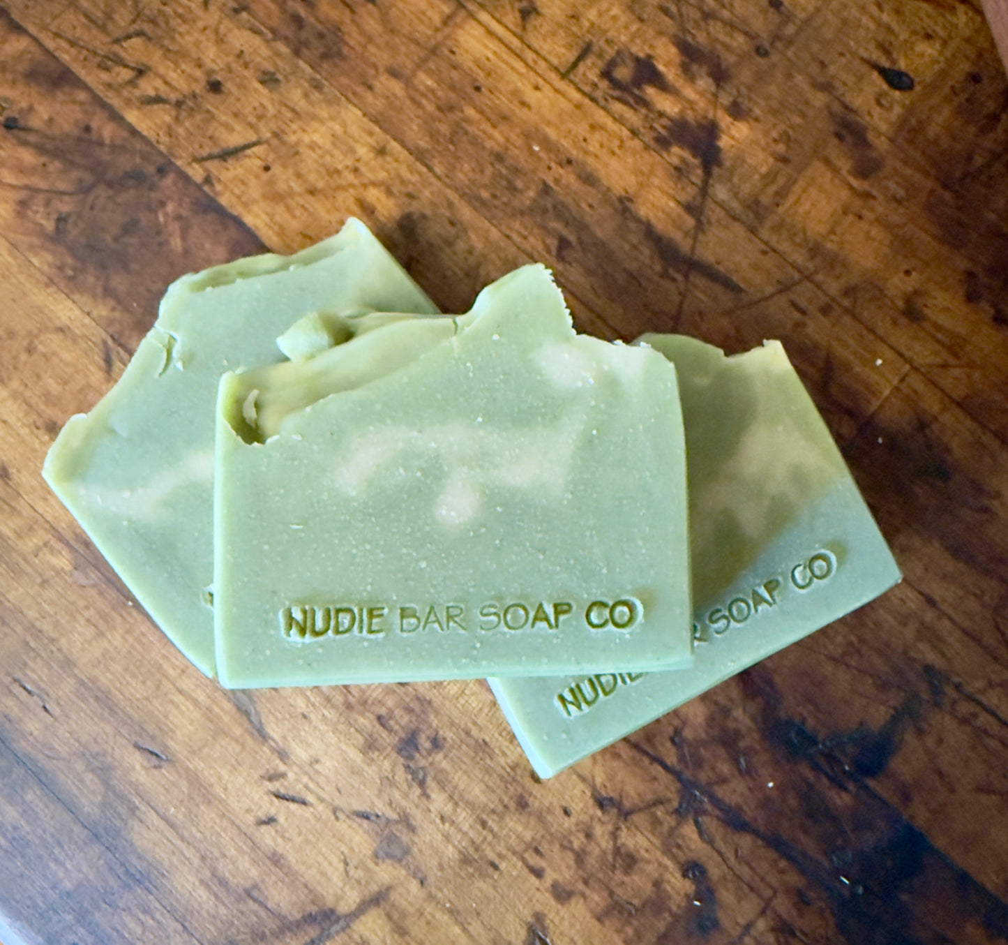 Three green bars of Nudie Bar Soap Co. soap on a wooden surface
